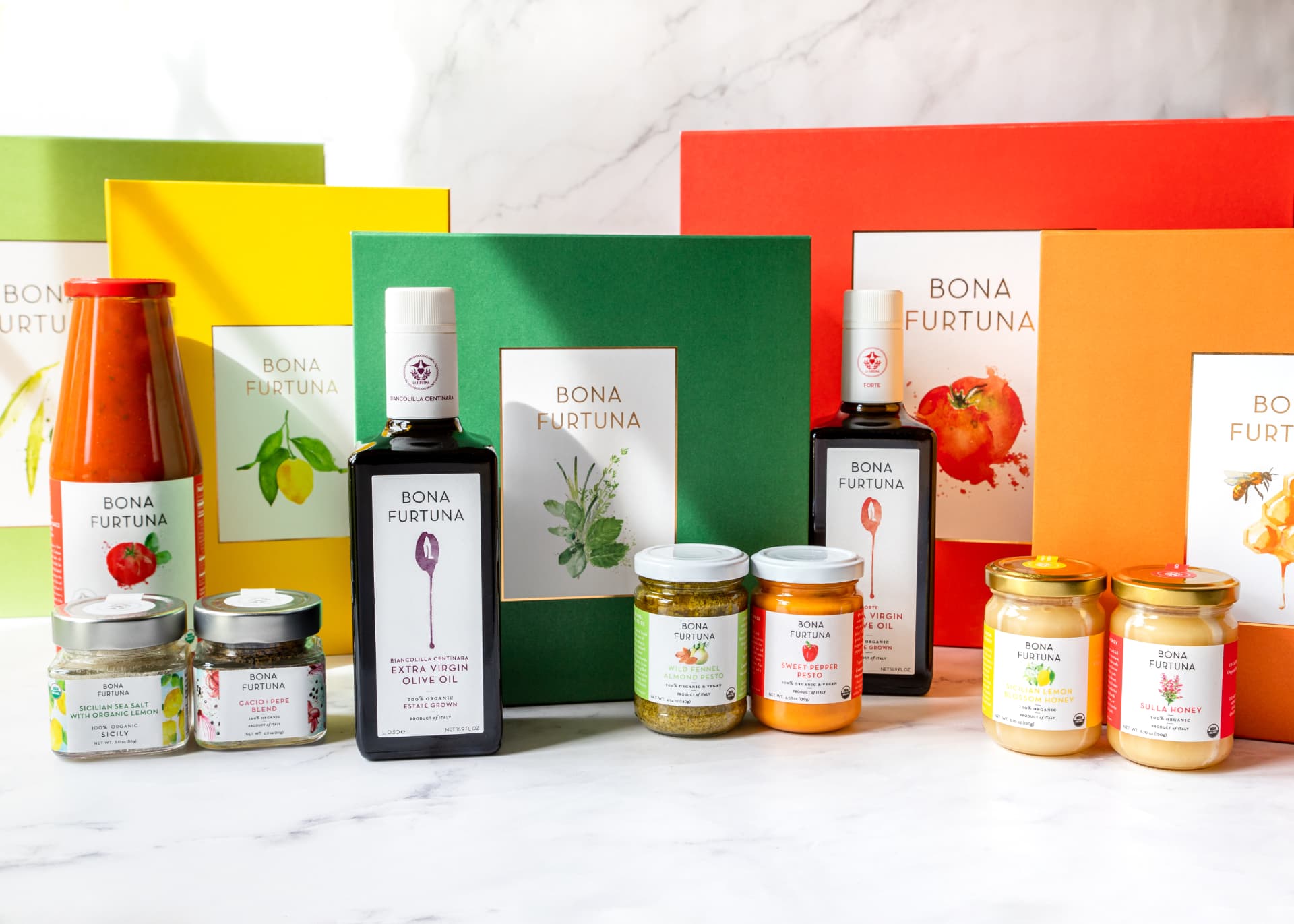Bona Furtuna extra virgin olive oil, pestos, honey and Sicilian seasonings arranged in front of colored gift boxes